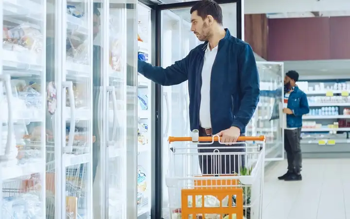 Mann kauft Tiefkühlkost, die hinter Termofrost® Glastüren im Supermarkt verstaut ist